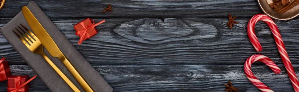 Vista superior de tenedor y cuchillo en servilleta con pequeños regalos y bastones de caramelo en mesa de madera oscura - foto de stock