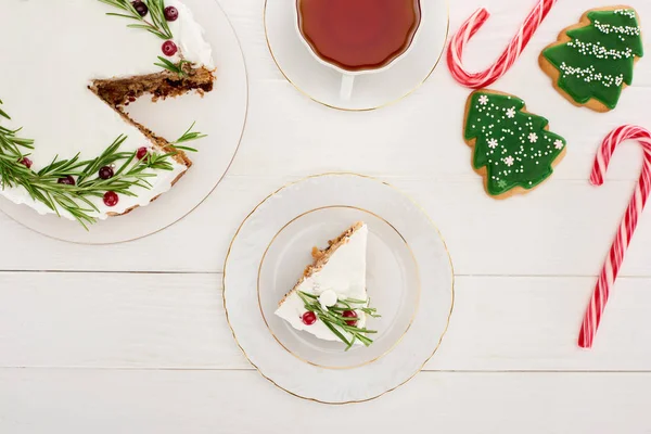 Vista dall'alto di torta di Natale, tazza di tè, bastoncini di zucchero e biscotti sul tavolo di legno bianco — Stock Photo