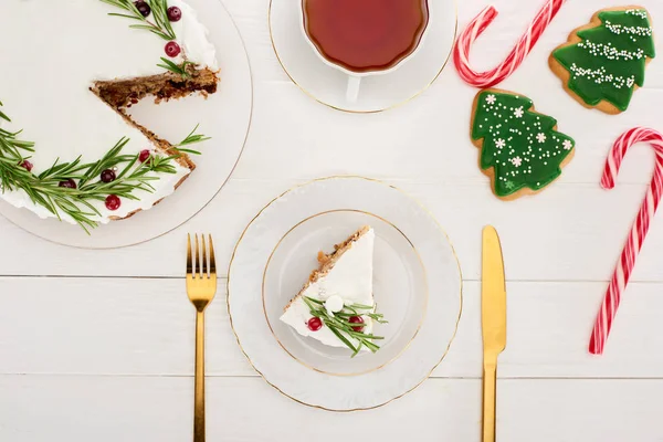 Vista superior del pastel de Navidad, té, galletas y bastones de caramelo en la mesa de madera blanca - foto de stock