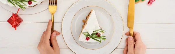 Vista recortada de niña sosteniendo tenedor y cuchillo para comer pastel de Navidad y galletas en mesa de madera blanca - foto de stock