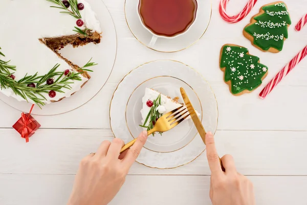 Vue recadrée de fille manger gâteau de Noël et biscuits sur table en bois blanc — Photo de stock