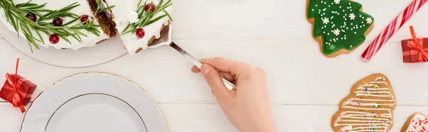 Vista recortada de chica con pastel de Navidad y galletas en mesa de madera blanca - foto de stock