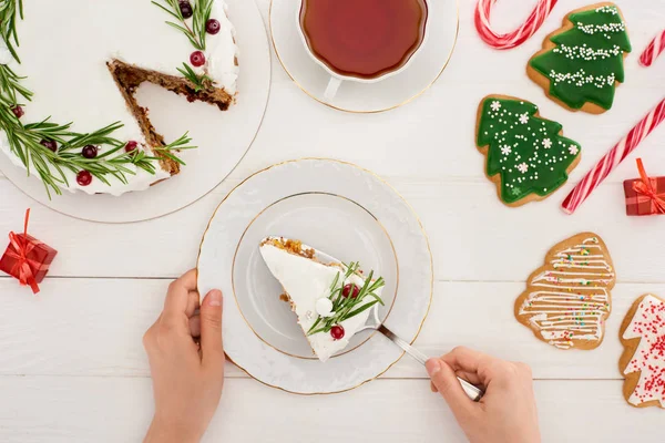 Vista recortada de la mujer con pastel de Navidad, galletas y té en la mesa de madera blanca - foto de stock