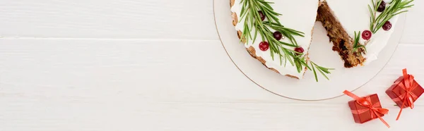 Vista superior del pastel de Navidad con romero y bayas rojas en la mesa de madera blanca con pequeños regalos - foto de stock