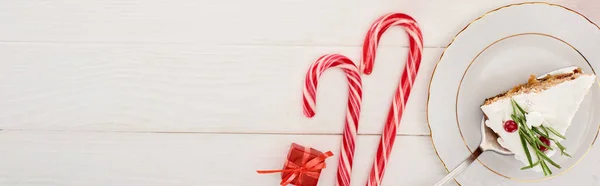 Vista superior del pedazo de pastel de Navidad con romero y arándanos sobre una mesa de madera blanca con bastones de caramelo y pequeño regalo - foto de stock