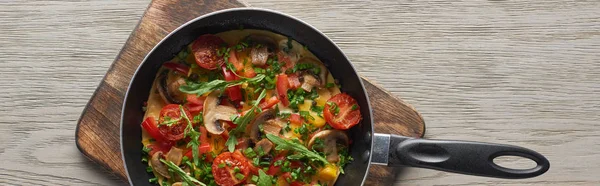 Vue du dessus de l'omelette aux légumes dans une poêle sur une planche de bois — Photo de stock