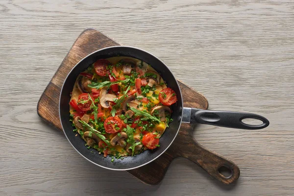 Top view of homemade omelet with vegetables in frying pan on wooden board — Stock Photo