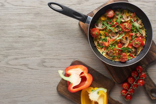 Vue du dessus de l'omelette maison dans une poêle sur une planche de bois avec poivrons et tomates cerises — Photo de stock