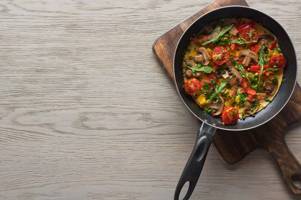 Top view of homemade omelet in frying pan on wooden board — Stock Photo