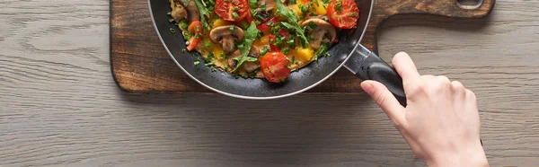 Top view of woman cooking omelet with mushrooms, tomatoes and greens on frying pan — Stock Photo