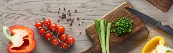 Top view of fresh bell peppers, cherry tomatoes and greens on wooden board with knife — Stock Photo