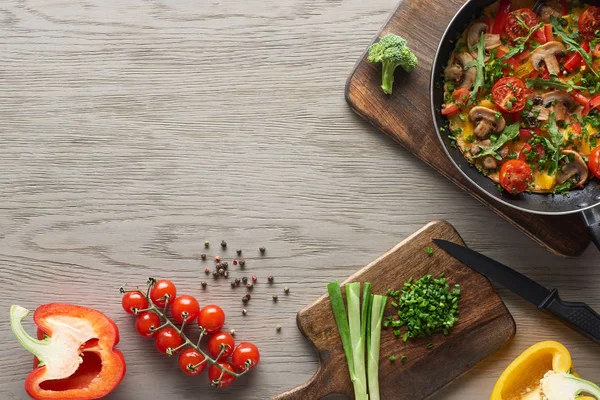 Vista superior da deliciosa omelete caseira na frigideira com tomate cereja e ingredientes na mesa — Fotografia de Stock