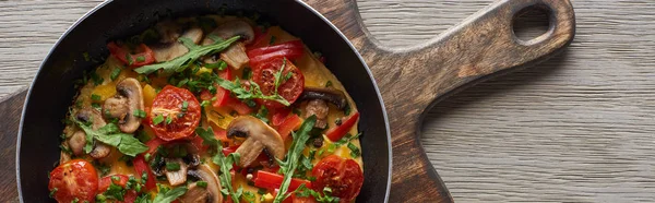 Top view of homemade omelet with vegetables and greens for breakfast in frying pan on wooden board — Stock Photo