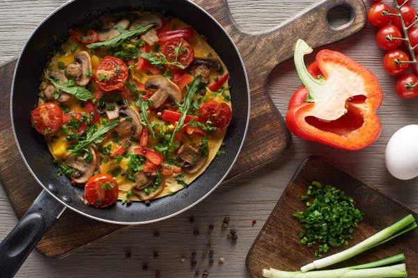 Vue de dessus de l'omelette maison délicieuse dans la poêle avec des ingrédients sur des planches en bois — Photo de stock