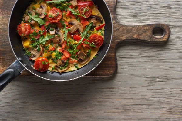 Top view of homemade omelet in frying pan on wooden board — Stock Photo