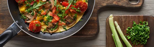 Vista superior da deliciosa omelete na frigideira com alho-porro fresco em tábuas de madeira — Fotografia de Stock