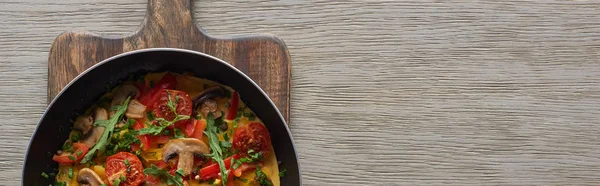 Vue de dessus de délicieuse omelette dans une poêle sur une planche de bois — Photo de stock