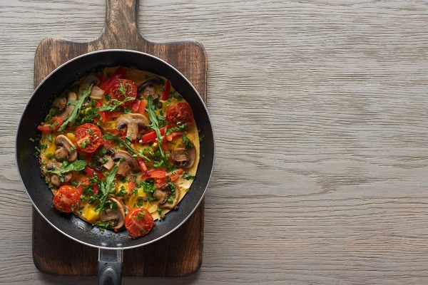 Top view of omelet with vegetables and greens in frying pan on wooden board — Stock Photo