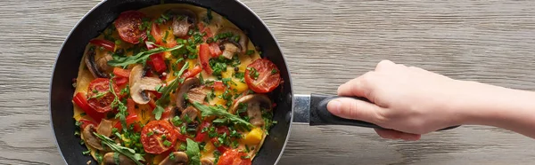 Cropped view of woman cooking omelet with mushrooms, tomatoes and greens on frying pan — Stock Photo