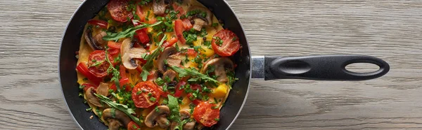 Top view of homemade omelet with vegetables and greens in frying pan on wooden table — Stock Photo