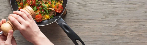 Cropped view of woman sprinkling pepper on omelet with mushrooms, tomatoes and greens — Stock Photo
