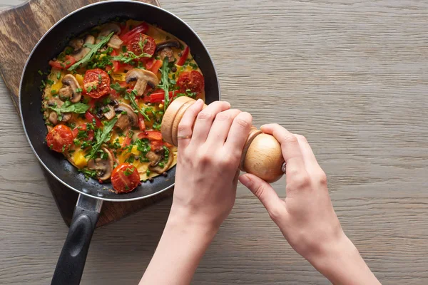 Vue du dessus de la femme saupoudrer de poivre sur l'omelette sur la poêle — Photo de stock