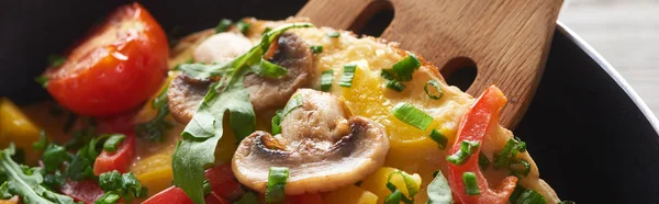 Close up of delicious omelet with vegetables and greens in frying pan with wooden shovel — Stock Photo