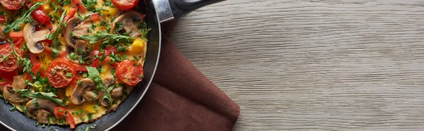 Top view of homemade omelet in frying pan on wooden table with napkin — Stock Photo