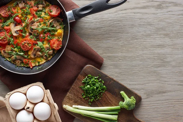 Top view of delicious homemade omelet in frying pan with ingredients on wooden table — Stock Photo