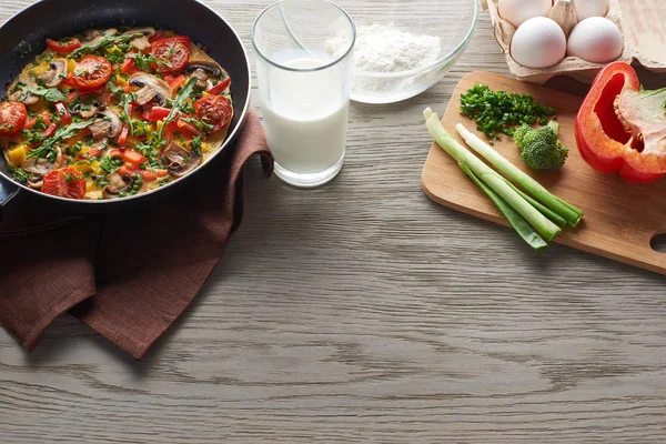 Delicious homemade omelet in frying pan with ingredients on table — Stock Photo