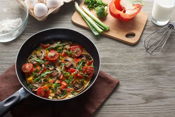 Tasty homemade omelet in frying pan with ingredients on table — Stock Photo