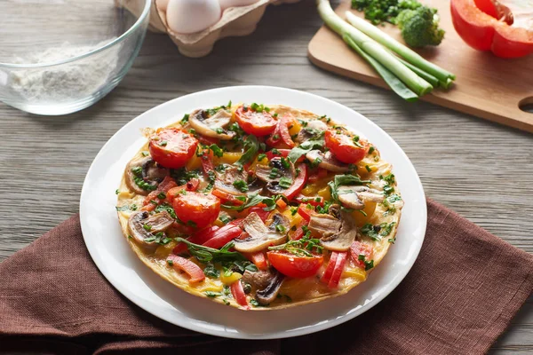 Frittata fatta in casa con verdure sul tavolo di legno con tovagliolo e ingredienti — Foto stock