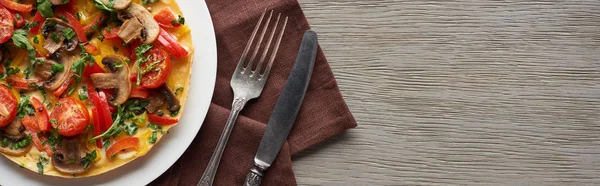 Top view of homemade omelet with vegetables on wooden table with fork, knife and napkin — Stock Photo