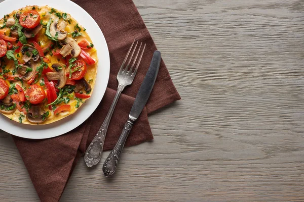 Vue de dessus de l'omelette délicieuse aux légumes sur une table en bois avec fourchette, couteau et serviette — Photo de stock