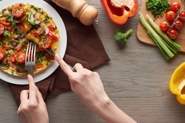 Vista cortada da mulher comendo na omelete da placa na mesa com ingredientes frescos — Fotografia de Stock