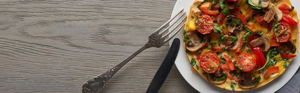 Vista dall'alto omelette su piatto con forchetta e coltello su tavolo in legno — Foto stock