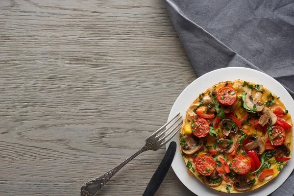 Vista dall'alto di deliziosa frittata fatta in casa con verdure sul tavolo di legno con forchetta, coltello e tovagliolo — Foto stock