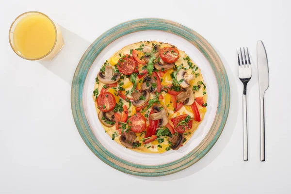 Teller mit hausgemachtem Omelett zum Frühstück auf weißem Tisch mit Glas Saft, Gabel und Messer — Stockfoto
