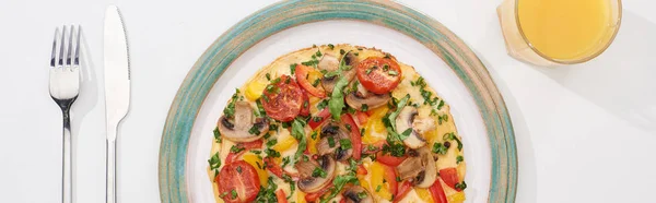 Vista superior da placa com omelete saboroso com tomates e cogumelos para o café da manhã na mesa branca com suco, garfo e faca — Fotografia de Stock