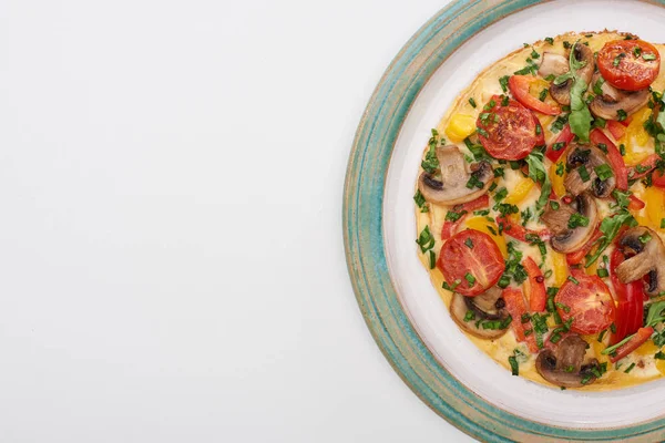 Vista superior del plato con sabrosa tortilla con tomates, verduras y champiñones para el desayuno en mesa blanca - foto de stock