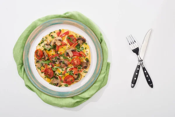 Vista superior da placa com omelete saboroso com tomates para o café da manhã na mesa branca com guardanapo, garfo e faca — Fotografia de Stock