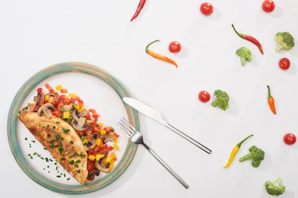 Vue du dessus de l'assiette avec omelette enveloppée maison aux légumes sur table blanche avec piments, tomates et brocoli — Photo de stock