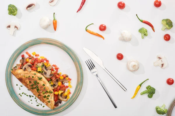 Vista superior da placa com omelete embrulhado caseiro com legumes na mesa branca com ingredientes, garfo e faca — Fotografia de Stock