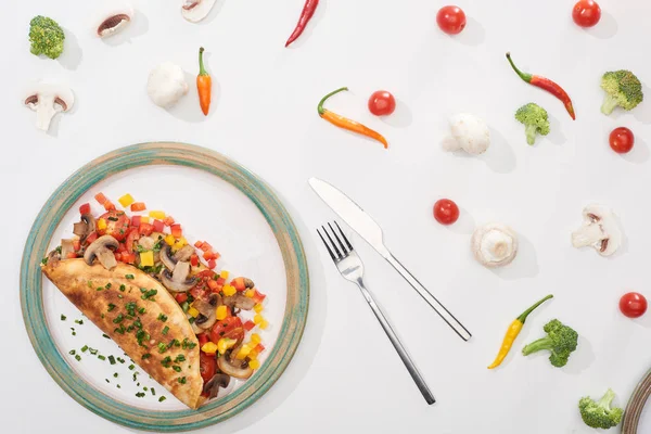 Top view of plate with homemade wrapped omelet with vegetables on white table with ingredients, fork and knife — Stock Photo