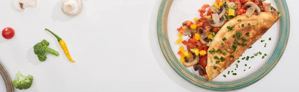 Верхний вид тарелки с домашним завернутым омлетом с овощами на белом столе с перцем чили, помидорами и брокколи — стоковое фото