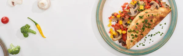 Top view of plate with homemade wrapped omelet with vegetables on white table with chili peppers, tomatoes and broccoli — Stock Photo