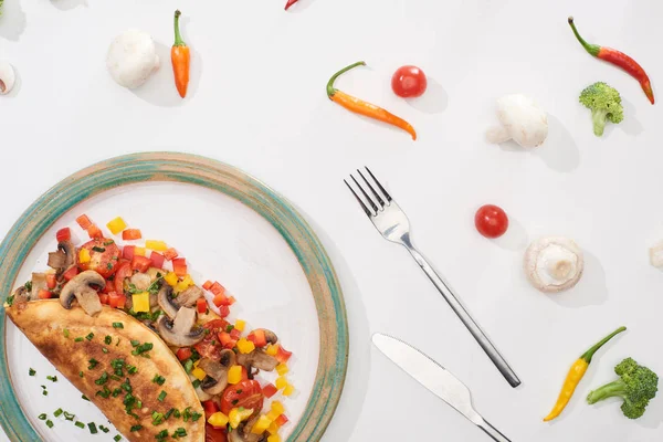 Вид сверху на тарелку с домашним завернутым омлетом с овощами на белом столе из свежих ингредиентов — стоковое фото