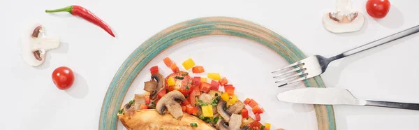 Top view of plate with yummy wrapped omelet with vegetables on white table with ingredients, fork and knife — Stock Photo