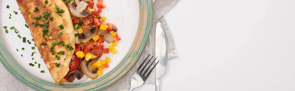 Vista superior del plato con tortilla envuelta con verduras sobre mesa blanca con tenedor y cuchillo - foto de stock