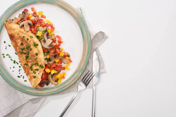 Vue du dessus de la plaque avec omelette enveloppée délicieuse aux champignons et poivrons sur table blanche avec fourchette et couteau — Photo de stock